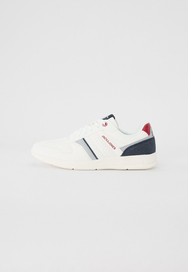 White athletic shoe with navy and red accents, textured upper, smooth sole, and subtle stripe design. Features branding on tongue and side.