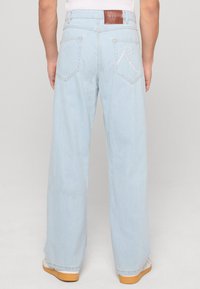 Vaaleansiniset leveälahkeiset farkut, jotka on valmistettu denimistä. Niissä on nahkapatteja vyötäröllä ja brodeerattu 'R' takataskussa.