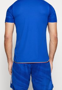 Niebieski sportowy T-shirt z krótkim rękawem, wykonany z gładkiego materiału. Posiada kolorową pasek u dołu. W zestawie z pasującymi niebieskimi szortami.