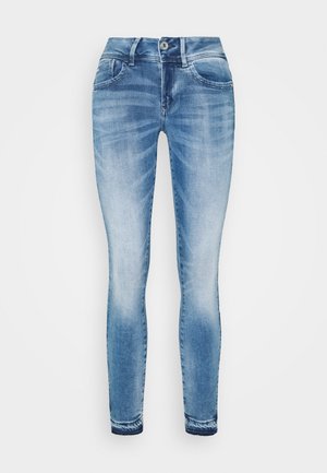 Blue denim skinny jeans with a faded wash, five pockets, and a classic button fly. Features stitching at the hem and a slim fit design.