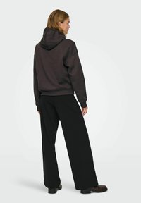 Donkergrijze hoodie met een grote capuchon en verlaagde schouders, gecombineerd met zwarte wijde broekspijpen. Soepele textuur met een ontspannen pasvorm.