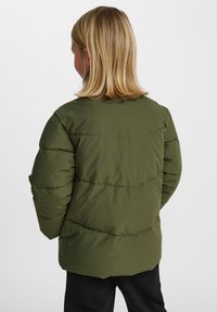 Vadderad jacka i olivgrön, med en enkel design, ribbad textur och horisontella sömmar över ryggen.