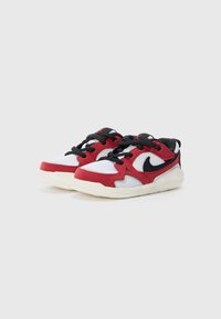 Scarpe sportive rosse e bianche con tomaia in rete, lacci neri e suola in gomma testurizzata; presenta il logo Nike sul lato.
