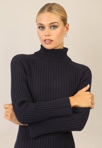 Marineblå ribbet turtleneck sweater med lange ærmer, der har en høj krave og en tætsiddende pasform, lavet af blødt, struktureret stof.