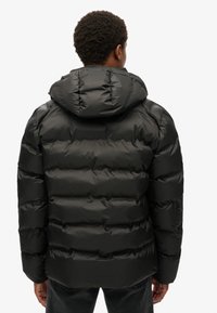 Svart puffjacka med huva, med en quiltad design, glänsande yta och elastiska ärmslut. Bakifrån visas den strukturerade formen.