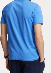 Kortärmad blå bomullströja med rundad halsringning, med en slät yta och en avslappnad passform. Bakifrån syns axelsömmarna och nederkanten.