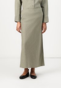 Jupe longue vert clair en tissu texturé, avec une taille cintrée et une coupe droite. Associée à des ballerines noires.