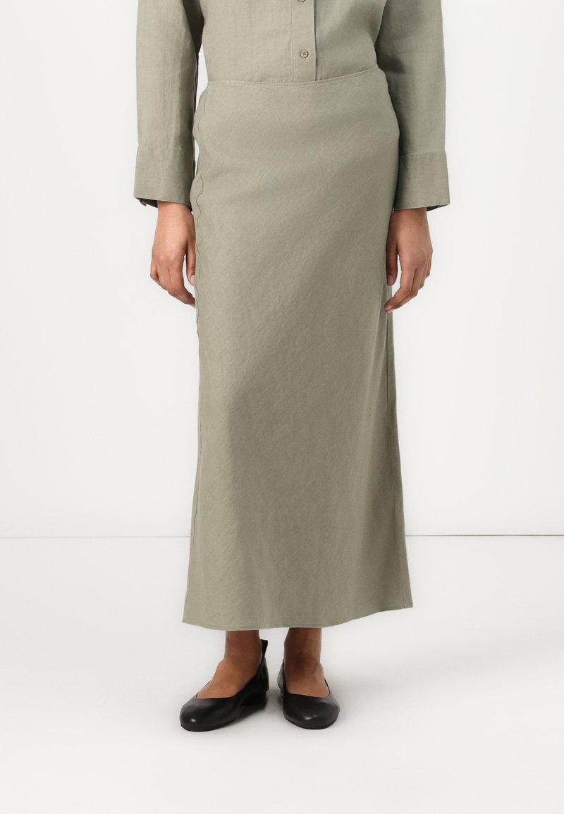 Jupe longue vert clair en tissu texturé, avec une taille cintrée et une coupe droite. Associée à des ballerines noires.