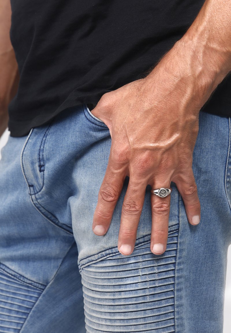 Ljusblå denimjeans har ribbade detaljer på låret, tillsammans med en svart t-shirt. En silverring bärs på höger hand.