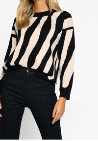 Suéter de rayas negro y beige de punto suave con cuello redondo y puños acanalados negros, combinado con jeans negros de cintura alta.