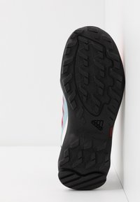 Musta kumipohja, jossa on tekstuurinen kuvio, sininen, punainen ja valkoinen synteettisestä materiaalista valmistetut yläosat. Tunnistettava adidas-logo näkyvissä.