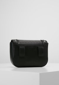 Svart läderbältesväska med silverstift och två bältesöglor, placerad på en vit plattform mot en enkel grå bakgrund.