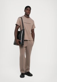 Beige t-skjorte med preget logo, kombinert med matchende beige bukser. Svart lær skulderveske. Glatt tekstur, avslappet passform.