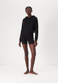 Svart kort zip-up hoodie med huva, matchad med svarta åtsittande shorts. Materialen verkar släta och elastiska, lämpliga för aktiv klädsel.