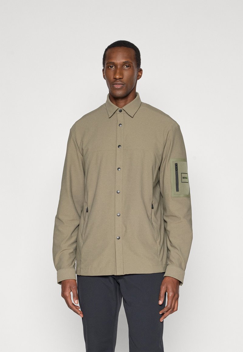 Ελαιόχρωμο μπουφάν φτιαγμένο από υφασμάτινο, υφή, με κουμπιά που ασφαλίζουν, τσέπη στο στήθος και ρυθμιζόμενο στρίφωμα. Περιλαμβάνει μία θηλή στο μανίκι.