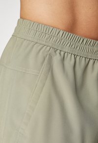 Light green, soft fabric shorts with an elastic waistband, featuring a side pocket and subtle stitching details for added durability.