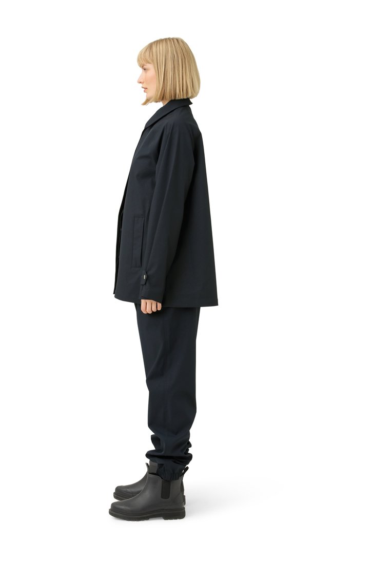 Giacca impermeabile della marina con tasche laterali, abbinata a pantaloni coordinati e stivali in gomma neri. Design semplice con vestibilità dritta.
