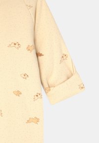 Gul babybody i mjuk bomull, med ett lekfullt kaninmönster och ljusblåa prickar. Korta ärmar med uppvikta fållar.