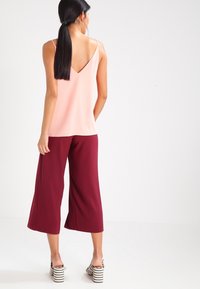 Top sin mangas de cuello en v color durazno combinado con pantalones anchos burdeos de pierna corta y sandalias de tacón bloque a rayas blancas y negras.