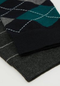 Dwie pary skarpet: jedna ma ciemnonawowe i turkusowe wzory w diamenty, druga jest jednolita w ciemnoszarym kolorze z cienkimi białymi paskami. Dzianinowa tekstura.