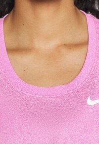 Vaaleanpunainen urheilu toppi, jossa on pyöreä kaula-aukko, teksturoitu kangas ja pieni valkoinen Nike-logo vasemmalla puolella.