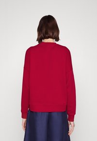 Sudadera roja de corte relajado, con cuello redondo y hombros caídos. La textura suave y los puños acanalados realzan el diseño.