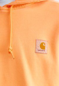 Oranje katoenen hoodie met een trekkoord, een zachte textuur en een vierkante patch met een geel logo en merknaam "Carhartt."
