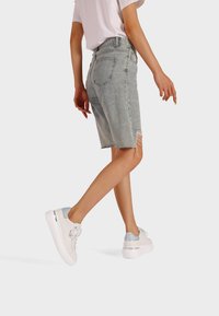 Shorts in denim azzurro chiaro con orlo sfrangiato, design a vita alta, abbinati a sneakers bianche e argentate. T-shirt semplice visibile sopra la vita.
