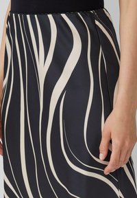 Zwarte en crèmekleurige rok met een patroon van golvende lijnen, een soepele textuur, een elastische tailleband en een close-up van de zoom en een hand.