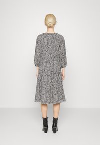 Musta-valkoinen kuviollinen mekko, jossa on kolme neljänneksen hihaa, kerroksellinen muotoilu ja rento leikkaus, yhdistettynä mustiin korokepohjaisiin nilkkasaappaisiin.