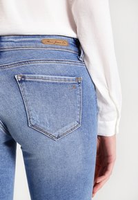 Ljust blå denimjeans med en figurnära design, med bakfickor och en brun läderetikett i midjan. Slät textur och klassisk form.