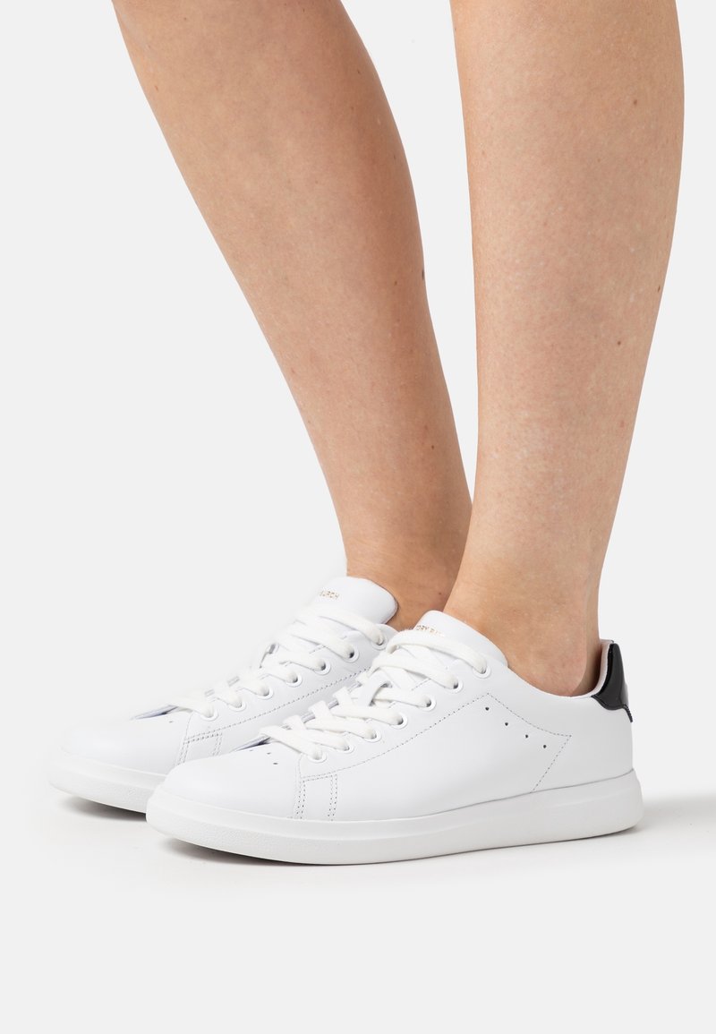 Baskets en cuir blanc avec un bout arrondi, fermées par des lacets à l'avant, et un accent noir au niveau du talon. Surface texturée avec des détails perforés.