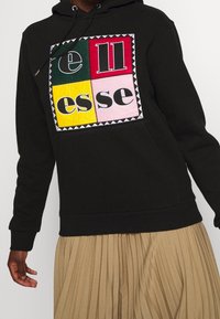 Černá mikina s kapucí a barevným čtvercovým logem s nápisem "ellesse" tučnými písmeny; zahrnuje kapuci se šňůrkami a měkkou tkaninu.