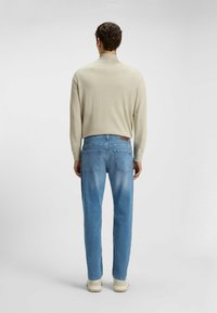 Light beige knit sweater with a high collar, paired with mid-blue denim jeans and cream sneakers, viewed from the back.