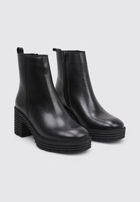 Bottes de cheville en cuir noir au design épuré, avec une fermeture éclair latérale et des talons blocs texturés comportant des rainures horizontales.