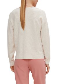 Pull en coton doux rose clair, coupe décontractée, épaules tombantes et ourlet côtelé. En arrière-plan, un pantalon assorti rose.