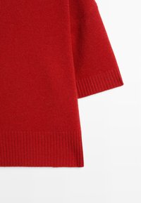 Czerwony sweter o gładkiej fakturze, z prążkowanymi detalami na brzegach i krótkimi rękawami. Miękka tkanina idealna do warstwowania.