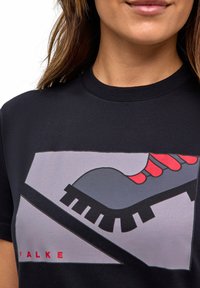Zwarte t-shirt met een grafisch ontwerp van een schoen met een grijze basis en rode accenten. De tekst "FALKE" staat in dikke rode letters onderaan.