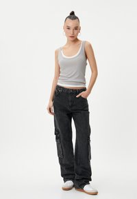 Zwarte denim cargo broeken met zijzakken, relaxte fit en een vervaagde textuur, gecombineerd met een grijze geribde tank top. Witte sneakers maken de look af.