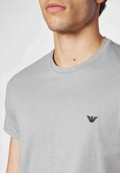 Graues Baumwoll-T-Shirt mit Rundhalsausschnitt und kurzen Ärmeln, mit einem kleinen schwarzen gestickten Logo auf der Brust.