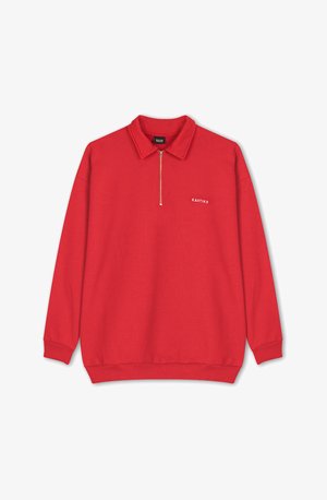 Punainen huppari, jossa on kaulus, puolivetoketju edessä, pitkät hihat ja ribattu resori. Edessä pieni valkoinen logo rinnassa. Pehmeä kangas.