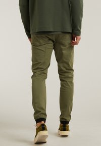 Pantalon de jogging kaki avec poignets élastiques, doté de deux poches arrière, d'une texture lisse et d'une coupe fuselée. Associé à des baskets en daim vert.