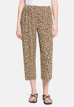 Frau trägt verkürzte, locker sitzende Hose mit braun-beigem Leopardenmuster und schwarze Sandalen mit goldenen Akzenten.