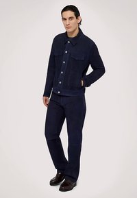 Mörkblå mockajacka och matchande byxor med knappstängning fram, två bröstfickor och avslappnad passform. Matchas med bruna skor.