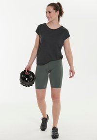 Svart kortärmad topp kombinerad med gröna cykelshorts. Ämnet håller en svart cykelhjälm och har på sig svarta cykelskor.