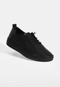 Chaussure décontractée noire avec dessus texturé, bout rond, semelle cousue et lacet élastique avec arrêt sur fond blanc.