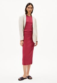 Lichtgekleurde linnen blazer over een aansluitend rood topje en een kokerrok. Open teen zwarte slides. Glad stof met een lichte glans, geen zichtbare patronen.