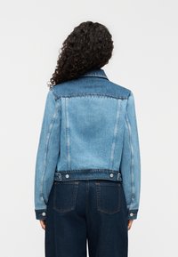 Ανοιχτό μπλε τζιν μπουφάν με σκούρο τζιν γιακά, κουμπιά τύπου snap στη μέση και πλαϊνές τσέπες. Διαθέτει κλασικό γιακά και στενή σχεδίαση.