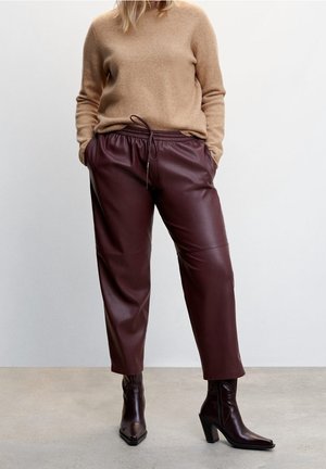 Burgundy faux leather pants with a drawstring waist, relaxed fit, and side pockets, paired with a beige cashmere sweater and dark heeled boots.