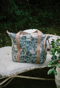 Blomster-mønstrede tote-tasker i grøn og pink, lavet af stof med brune stropper, et logomærke og en struktureret form.